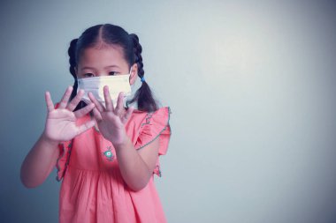 Tıbbi maske takan Asyalı bir kız alkol jeli kullanarak temizlik yaptıktan sonra ellerine bakıyor. Coronavirüs salgınını durdurmak için sosyal mesafeleri korumak, yüz maskeleri takmak ve evi terk etmek zorundalar..