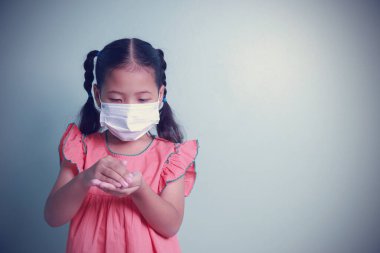 Koronavirüs Covid-19 'u korumak için alkol jeli kullanarak tıbbi maske takan Asyalı kız. Coronavirüs salgınını durdurmak için sosyal mesafeleri korumalı, yüz maskeleri takıp evden ayrılmalılar..