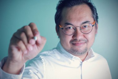 Asyalı işadamı, elinde kalem tutarak mutlu bir yüz ifadesi takınıyor. Gözlük takan, kendinden çok emin, mutluluktan gülümseyen, fotokopi çekilen kameraya bakan bir adam..