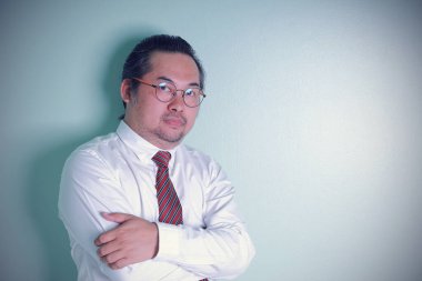 Asyalı işadamı yeşil arka planda çapraz silahlarla duruyor. Gözlük takan bir adam başarılı olacağına inanıyor. Portre yakın çekim adamı fotokopi alanıyla kameraya bakıyor..