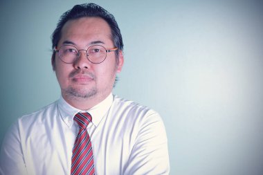 Asyalı işadamı fotokopi makinesiyle kameraya bakıyor. Yeşil arka planda başarılı olmak isteyen gözlüklü adam. Asyalı işadamı çapraz silahlarda ihtiyatlı görünüyor.