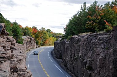 Dağ yolunun yüksek açılı manzarası. Kayalarla kaplı manzara, sonbahar yapraklarının rengi ve sonbaharda asfalt yolların güzelliği. Dağlarda otoyol. Ulaşım