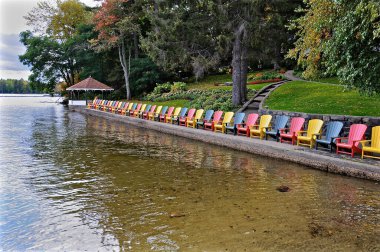  Turizm merkezinin göl kıyısındaki teras çardağının önünde çok renkli Muskoka sandalyeleri..