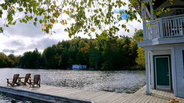 Kayıkhanenin rıhtımından göl manzarası. Gölün karşısında yeşil ağaçların arasına kurulmuş bir kulübe var..