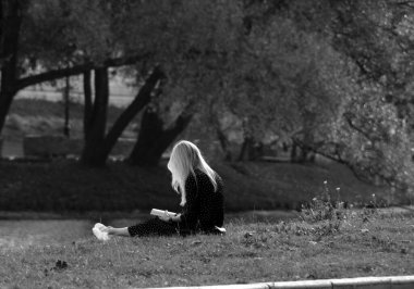 Sarışın bir kız pazar öğleden sonra göletin kenarında çimlerin üzerinde otururken bir kitapla dinleniyor. Tek renkli fotoğraf..