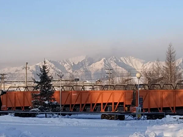 Image of freight railway cars on the background of the Kodar ridge. The air temperature at this time is minus 35 degrees Celsius.
