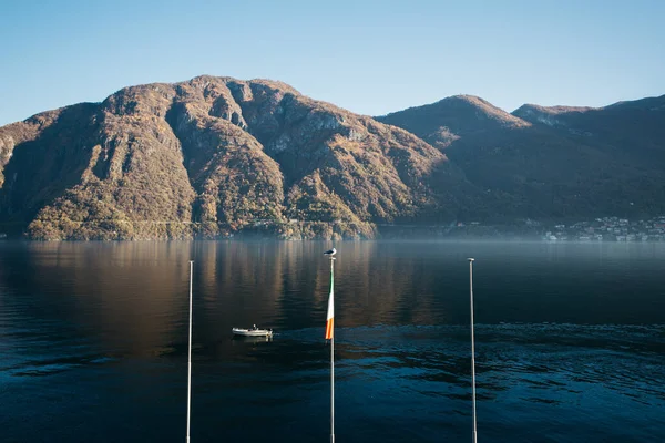 Bandiere e bandiera d'Italia. Il gabbiano siede sul pennone. Bella vista sulle montagne e sul lago su cui naviga la barca . — Foto Stock