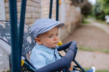 Bahçedeki bebek arabasında şapkası olan güzel bir çocuk.