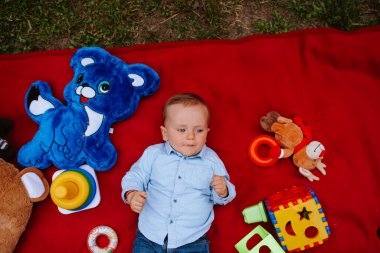 Bahçede güzel beyaz bir çocuk battaniyede oyuncaklarla oynuyor.