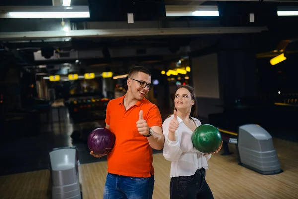 A beautiful loving couple on a bowling alley with balls giving thumb up. Love and recreation