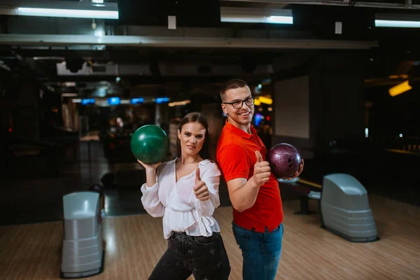 A beautiful loving couple on a bowling alley with balls giving thumb up. Love and recreation