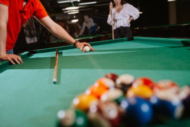 Kırmızı tişörtlü beyaz bir adam topları bilardo masasına yerleştiriyor. Eğlence zamanı. 