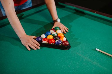 Kırmızı tişörtlü beyaz bir adam topları bilardo masasına yerleştiriyor. Eğlence zamanı. 