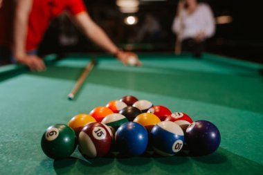 Kırmızı tişörtlü beyaz bir adam topları bilardo masasına yerleştiriyor. Eğlence zamanı. 