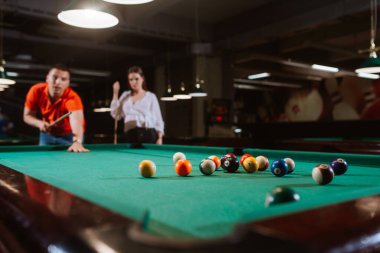  Kırmızı tişörtlü genç beyaz bir adam yanında bir kız dururken bilardo oynuyor. Eğlence zamanı.