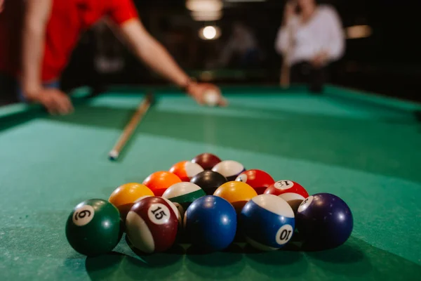 Kırmızı tişörtlü beyaz bir adam topları bilardo masasına yerleştiriyor. Eğlence zamanı. 