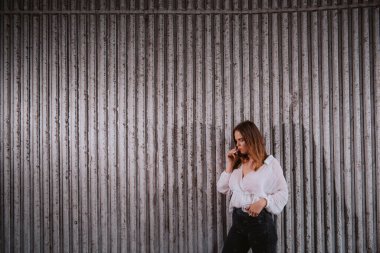 Beyaz tişörtlü güzel beyaz bir kız bir duvarın önünde duruyor ve puro içiyor.