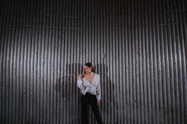 Beyaz tişörtlü güzel beyaz bir kız, tırtıklı bir duvarın önünde duruyor.