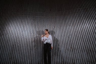 Beyaz tişörtlü güzel beyaz bir kız, tırtıklı bir duvarın önünde duruyor.