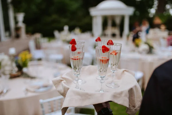 The waiter serves a glass of champagne with strawberries on a tray