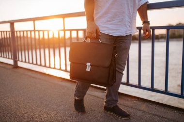 Köprüde orta yaşlı bir işadamının elinde taşınan siyah evrak çantasının yakın çekimi.