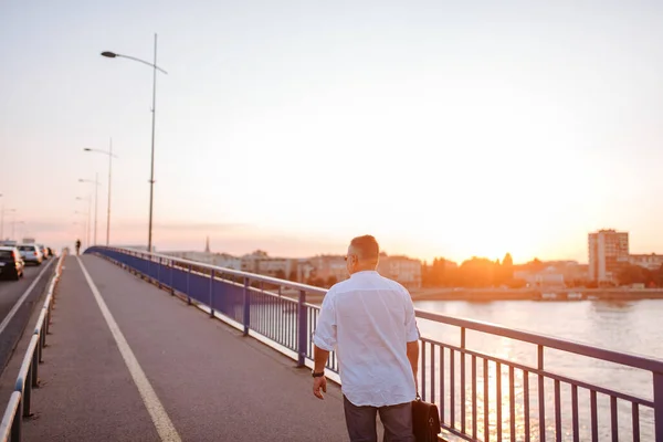 Stock image A middle-aged caucasian businessman with glasses, in a white shirt and a black briefcase in his hand walks on the bridge