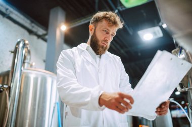 Beyaz giysi üretim makinesi üretimi konusunda uzman beyaz tenli erkek profesyonel teknoloji uzmanı gıda fabrikasında ve kalite kontrolü yapıyor ve kontrol listesi tutuyor. Gıda endüstrisindeki üretimi kontrol etmek.