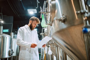 Beyaz giysi üretim makinesi üretimi konusunda uzman beyaz tenli erkek profesyonel teknoloji uzmanı gıda fabrikasında ve kalite kontrolü yapıyor ve kontrol listesi tutuyor. Gıda endüstrisindeki üretimi kontrol etmek.