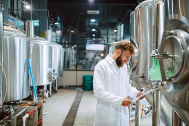 Beyaz giysi üretim makinesi üretimi konusunda uzman beyaz tenli erkek profesyonel teknoloji uzmanı gıda fabrikasında ve kalite kontrolü yapıyor ve kontrol listesi tutuyor. Gıda endüstrisindeki üretimi kontrol etmek.