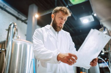 Beyaz giysi üretim makinesi üretimi konusunda uzman beyaz tenli erkek profesyonel teknoloji uzmanı gıda fabrikasında ve kalite kontrolü yapıyor ve kontrol listesi tutuyor. Gıda endüstrisindeki üretimi kontrol etmek.