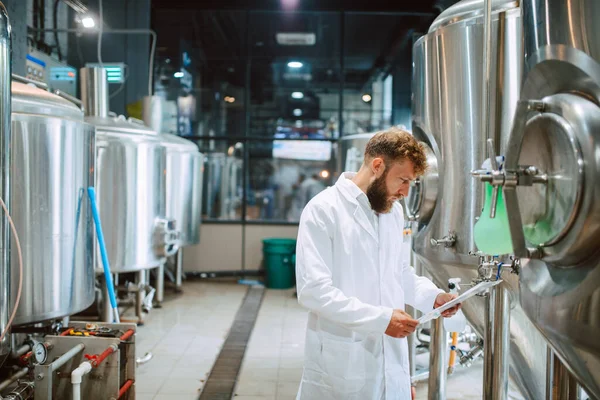 Beyaz giysi üretim makinesi üretimi konusunda uzman beyaz tenli erkek profesyonel teknoloji uzmanı gıda fabrikasında ve kalite kontrolü yapıyor ve kontrol listesi tutuyor. Gıda endüstrisindeki üretimi kontrol etmek.