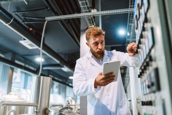  Eczacılık veya gıda fabrikasında duran beyaz üniformalı beyaz üniformalı profesyonel beyaz teknoloji uzmanı - üretim tesisi tablet bilgisayar kullanarak verimliliği ve kaliteyi kontrol ediyor.