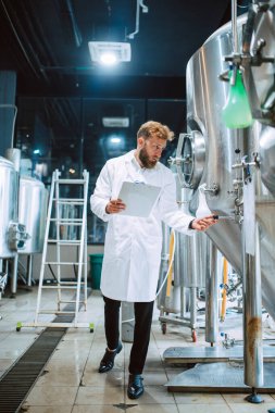 Beyaz giysi üretim makinesi üretimi konusunda uzman beyaz tenli erkek profesyonel teknoloji uzmanı gıda fabrikasında ve kalite kontrolü yapıyor ve kontrol listesi tutuyor. Gıda endüstrisindeki üretimi kontrol etmek.