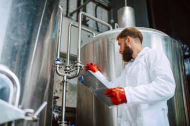 Beyaz giysi üretim makinesi üretimi konusunda uzman beyaz tenli erkek profesyonel teknoloji uzmanı gıda fabrikasında ve kalite kontrolü yapıyor ve kontrol listesi tutuyor. Gıda endüstrisindeki üretimi kontrol etmek.