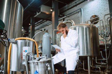  Eczacılık ya da gıda fabrikasında beyaz üniforma konusunda profesyonel Kafkasyalı teknoloji uzmanı. Üretim tesisi verimliliği ve kaliteyi tablet kullanarak kontrol ediyor. 