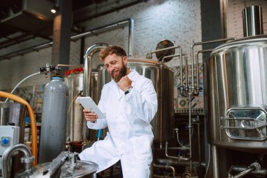  Eczacılık ya da gıda fabrikasında beyaz üniforma konusunda profesyonel Kafkasyalı teknoloji uzmanı. Üretim tesisi verimliliği ve kaliteyi tablet kullanarak kontrol ediyor. 