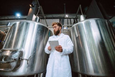  Eczacılık ya da gıda fabrikasında beyaz üniforma konusunda profesyonel Kafkasyalı teknoloji uzmanı. Üretim tesisi verimliliği ve kaliteyi tablet kullanarak kontrol ediyor. 