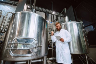  Eczacılık ya da gıda fabrikasında beyaz üniforma konusunda profesyonel Kafkasyalı teknoloji uzmanı. Üretim tesisi verimliliği ve kaliteyi tablet kullanarak kontrol ediyor. 