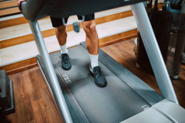 Spor salonundaki koşu bandında antrenman yapan ve koşan genç kaslı beyaz bir sporcunun bacaklarına yakın çekim. COVID 'e karşı koruma - 19 koronavirüs