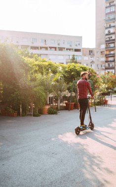 Şehirde elektrikli scooter kullanan yakışıklı bir adam.