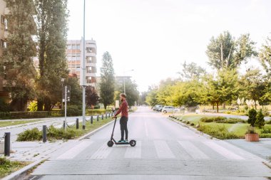 Şehirde elektrikli scooter kullanan yakışıklı bir adam.