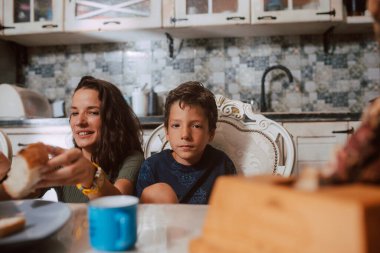 Güzel bir beyaz anne ve iki oğlu mutfaktaki masada kahvaltı yapıyorlar. Anne ve çocuklar mutfakta.
