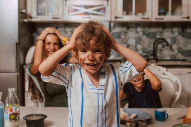 Mutfaktaki bir masada oturan sevimli, küçük, pis beyaz bir çocuk ve anne ile kardeşi onun arkasında oturuyorlar. Anne ve çocuklar kahvaltı yapar.