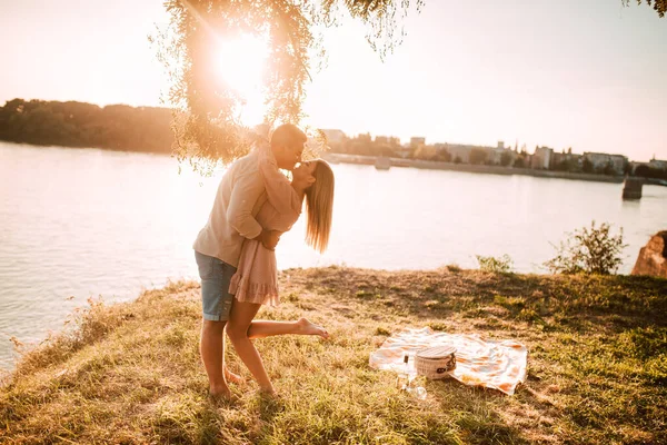 日落时 一个美丽的高加索金发女人和一个高加索男人站在河边亲吻 在迷人的夕阳下 一对浪漫的情侣 — 图库照片