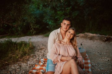 Çekici sarışın, beyaz bir kadın sahilde bir adamın kollarında yatıyor. Nehir kenarında piknik yapan sevgi dolu bir çift.