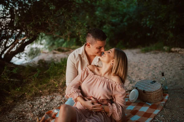 パステルピンクのドレスを着た魅力的な女性と ビーチの毛布にキスをする男 川のピクニックで愛しのカップル — ストック写真