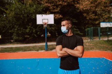 Açık hava basketbol sahasında duran kaslı, beyaz yüzlü bir sporcunun profili. Coronavirus koruması COVID - 19
