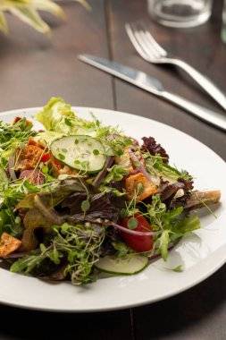 Beyaz tabakta sıralanmış sebzeli yeşil salata ve ahşap masa bardakları