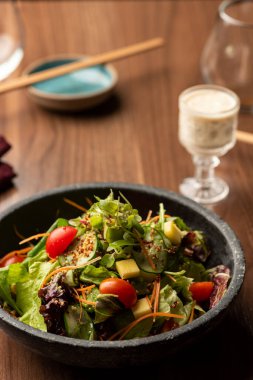 Yeşil salata ile marul roka domatesleri seramik kasede ve arka planda salata sosu.