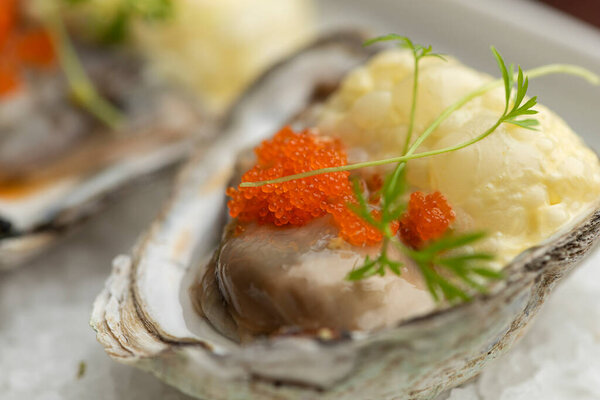 Oysters garnished with red caviar on salt and plate. Blurred background with wine corks
